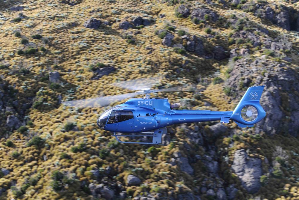 View from inside the cockpit in flight, alongside a second Tropic Air helicopter over the highlands