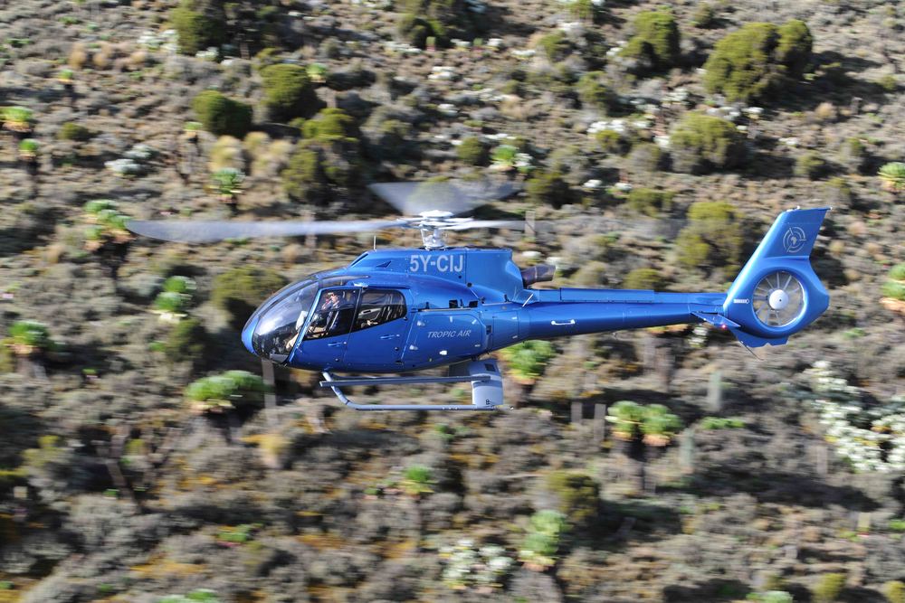 Tropic Air helicopter banking low over scrub-covered terrain